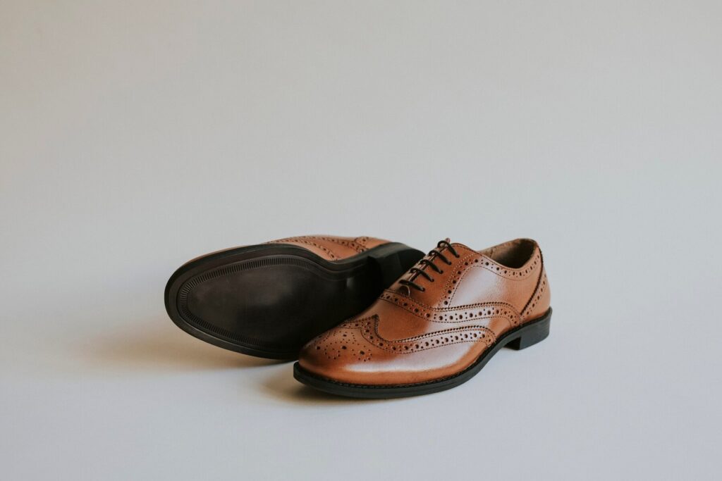 A pair of elegant brown leather brogue shoes on a pale background.