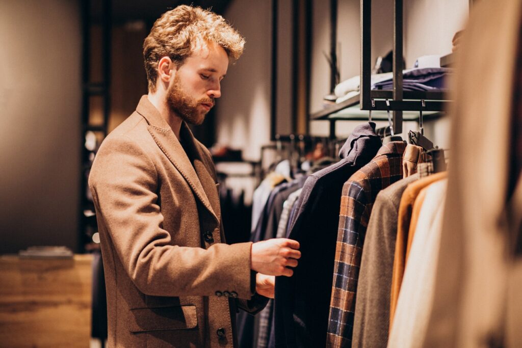 A man in a stylish brown coat browsing clothes in a chic boutique clothing store.