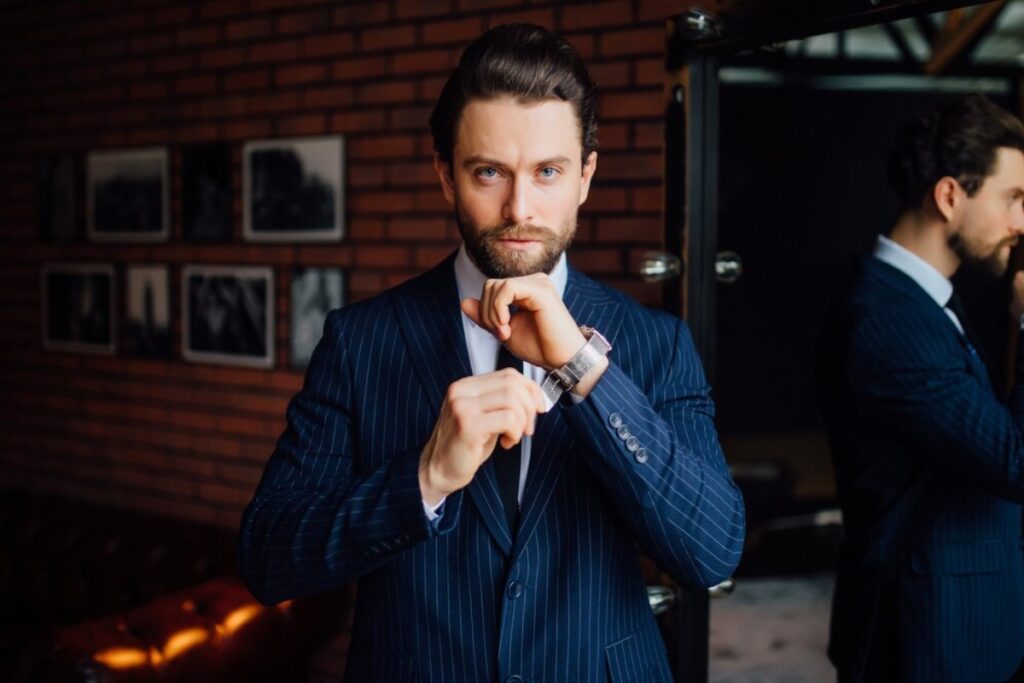 1. A man in a suit is adjusting his tie, standing confidently with a focused expression.