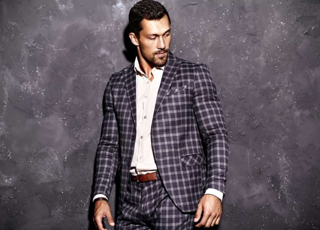A man in a suit and tie stands confidently against a plain wall, exuding professionalism and poise.