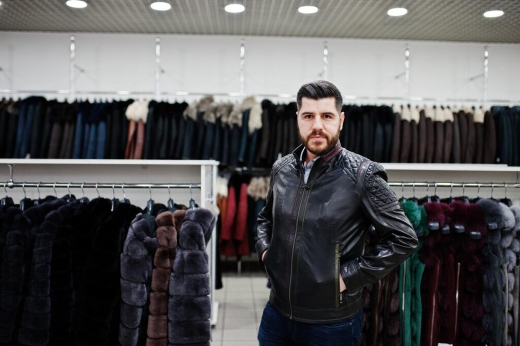 A man stands in front of a rack displaying various fur coats, showcasing a selection of luxurious outerwear.
